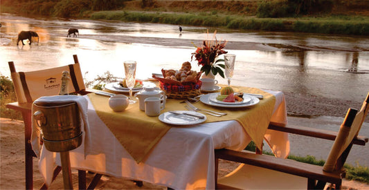 Dining table set for a meal by a river with scenic view on  luxury safari game drives in Masai Mara