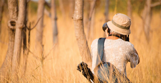 Person walking through tall grass with a hat and backpack in a natural setting