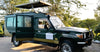 Green safari vehicle hire for Kenya game drives with an open roof on a road, parked near trees