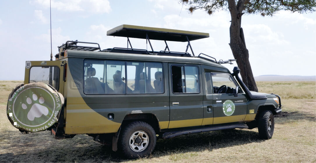 Large green off-road vehicle with a spare tire and an open roof near tree on a savannah in Kenya