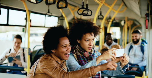 Two people sitting on a bus, looking at a phone together.