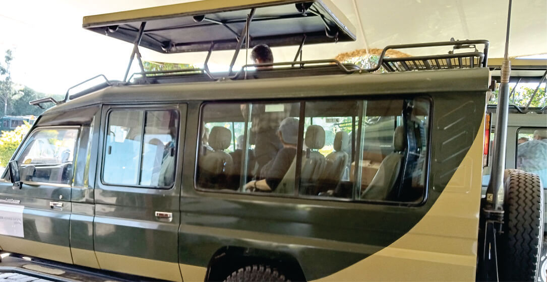 Green safari vehicle with open roof, driver guide and people inside, parked outdoors for rental safari holidays in Kisumu