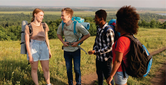 Four friends with backpacks standing in a grassy field with a scenic background