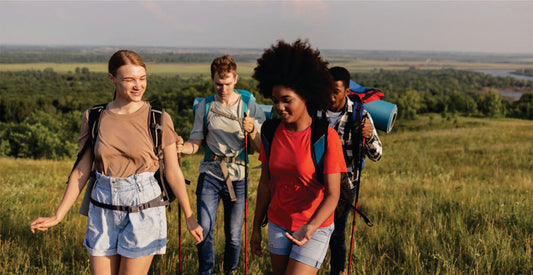 Four friends hiking through a scenic landscape with backpacks.
