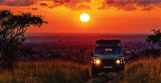 Jeep on a night safari game drive in Masai Mara at sunset with an orange sky and grassy landscape.