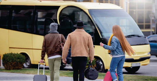 Three people with luggage walking towards a yellow transfer bus on affordable group transfer from Nairobi to Masai Mara