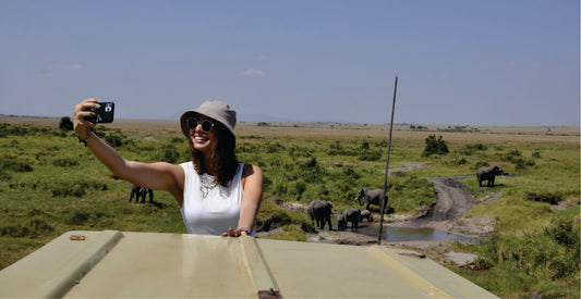 Woman taking a selfie with elephants in the background on a safari vehicle.