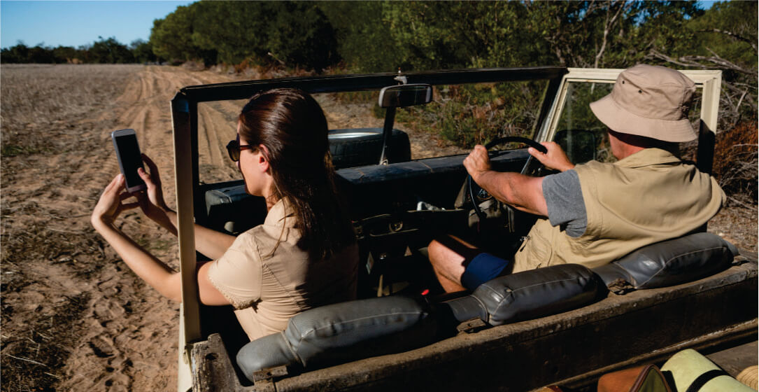 A guide and woman showing a camera in a jeep on Ol Pejeta Conservancy Kenya Safari Game Drive in a dirt road with trees in the background
