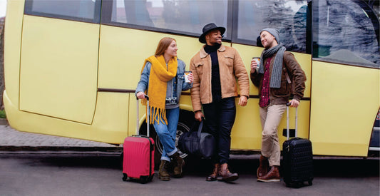 Three people with luggage standing in front of a yellow transfer bus on affordable group transfer from Nairobi to Masai Mara