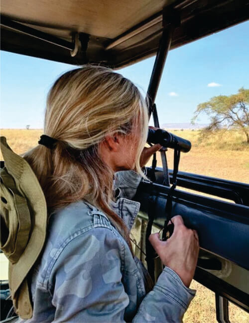 White Lady inside a safari jeep on game drive observing a game through a binocular in Masai Mara National Reserve