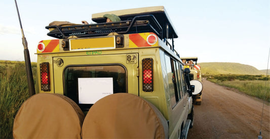 Back view of a yellow off-road transfer safari vehicle on a dirt road with a clear sky.