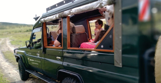 Green off-road vehicle with open doors, showing people inside, on a dirt road on Masai Mara family safari vehicle hire for Kenya