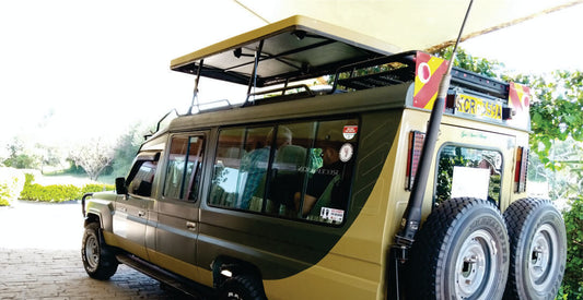 People sitting inside Masai Mara Kenya safari vehicle for hire with large wheels and roof top on a paved road in Kenya