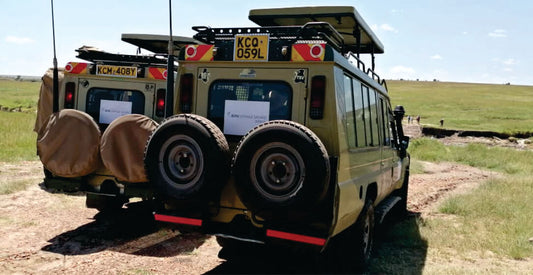 Large two off-road vehicles with spare tires on a dirt road in a grassy area with an open roof on safari in kenya