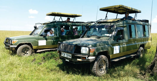 Two green safari vehicles with driver guides and open tops on a grassy field for Amboseli safari vehicle rental Kenya