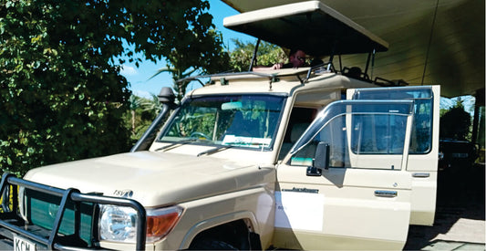Beige jeep safari vehicle with open roof and roof rack parked at a Nairobi Hotel, awaiting to transfer guests in Kenya.