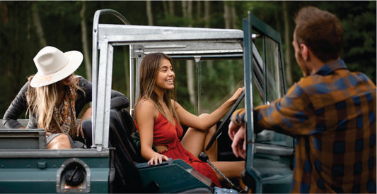 Two women and a man in a safari jeep vehicle for hire with a forest background